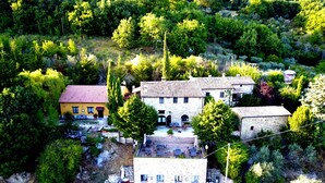 Il s'agit d'une propriété située sur une colline, comprenant plusieurs bâtiments, dont une maison en pierre avec un toit rouge et un bâtiment jaune. On y trouve des espaces extérieurs aménagés avec des tables et des chaises.
