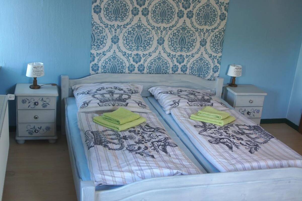 Un dormitorio con dos camas, cada una con colcha estampada y toalla verde. Hay dos mesitas de noche con lámparas y un aparador con cajones.