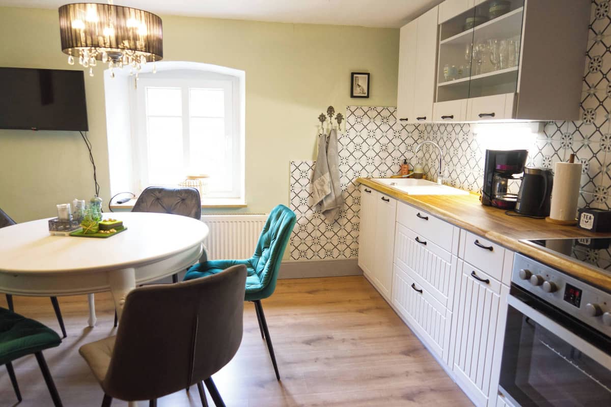 Una cocina con armarios blancos, encimera de madera, horno empotrado y comedor con mesa redonda y sillas.