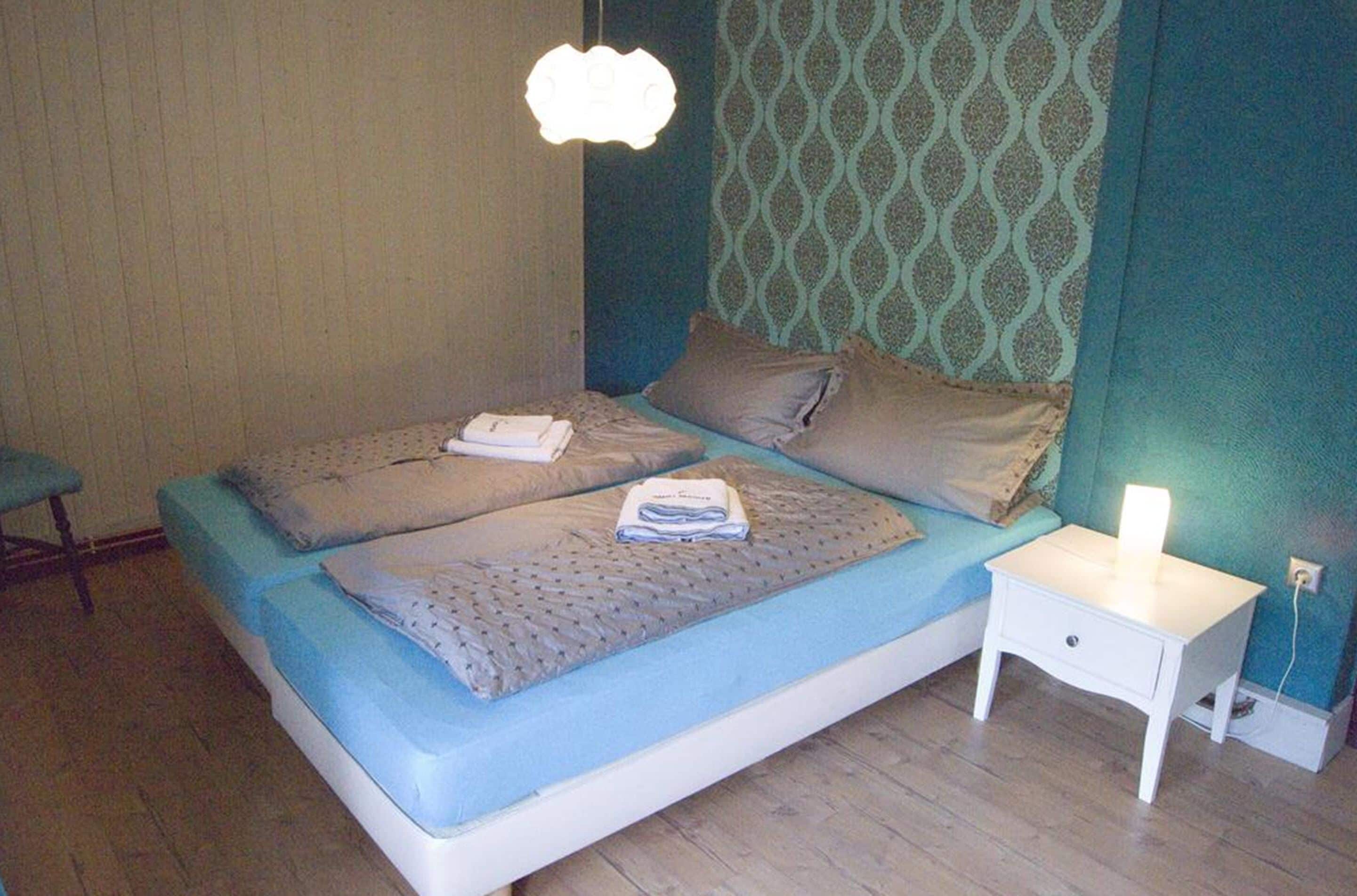 En dubbelsäng med ett blått madrass och kuddar, ett sängbord med en lampa och en vägg med ett mönster.