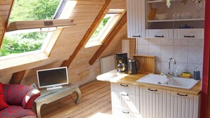 Kodikas ullakkohuone, jossa on kattolyhty, sänky, työpöytä ja pieni keittiönurkkaus.