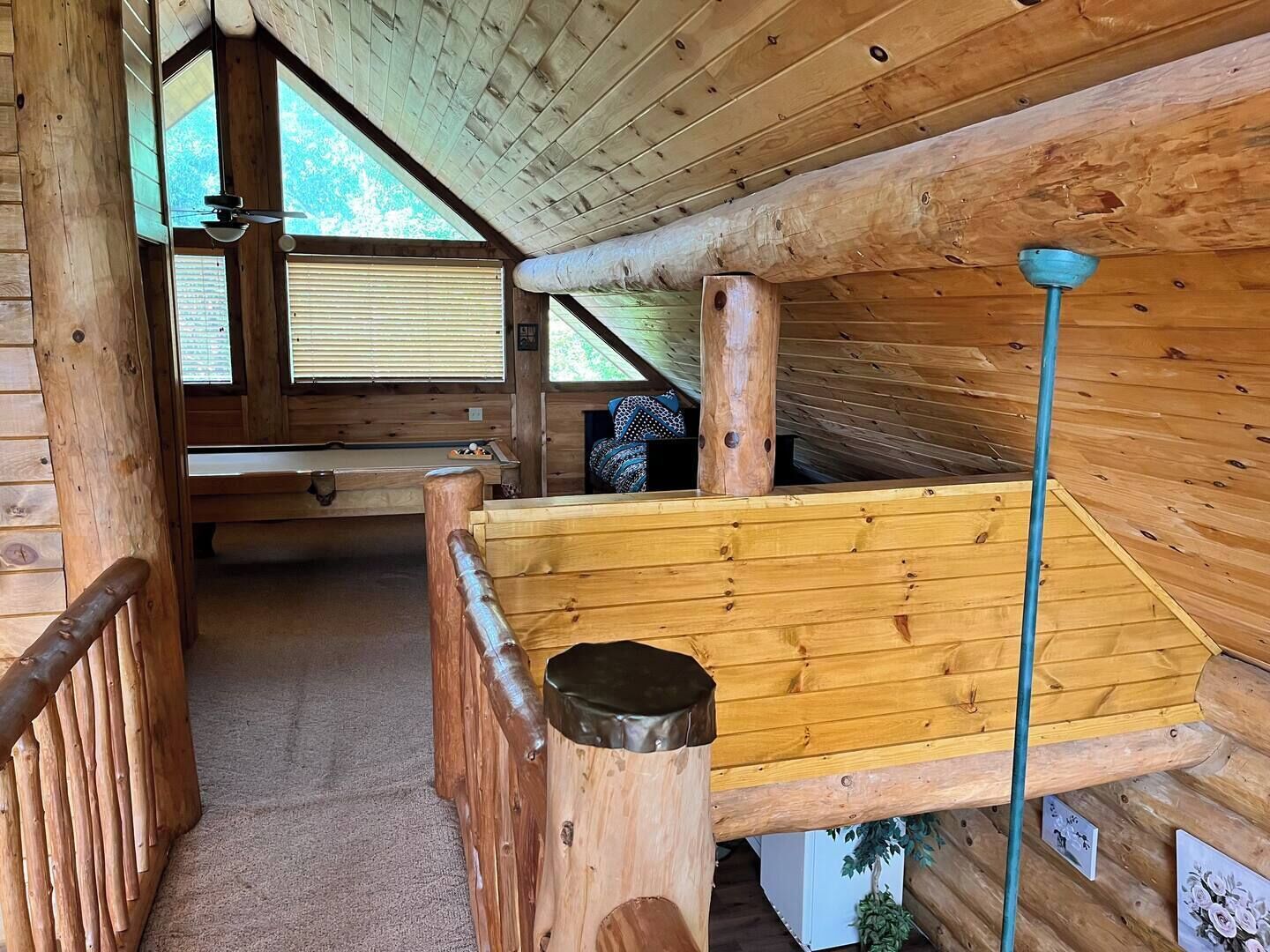 A wooden cabin interior with a pool table, a ceiling fan, and a staircase.