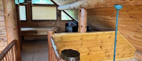 A wooden cabin interior with a pool table, a ceiling fan, and a staircase.