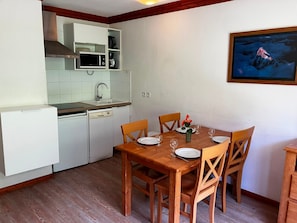 A compact kitchen with a microwave, sink, and dishwasher. A wooden dining table with chairs is set for two, with plates and glasses. - Appart cosy et charmant à 50m des remontées (Val-Cenis)