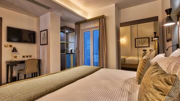 A hotel room with a large bed, a desk, a chair, a TV, and a wardrobe.