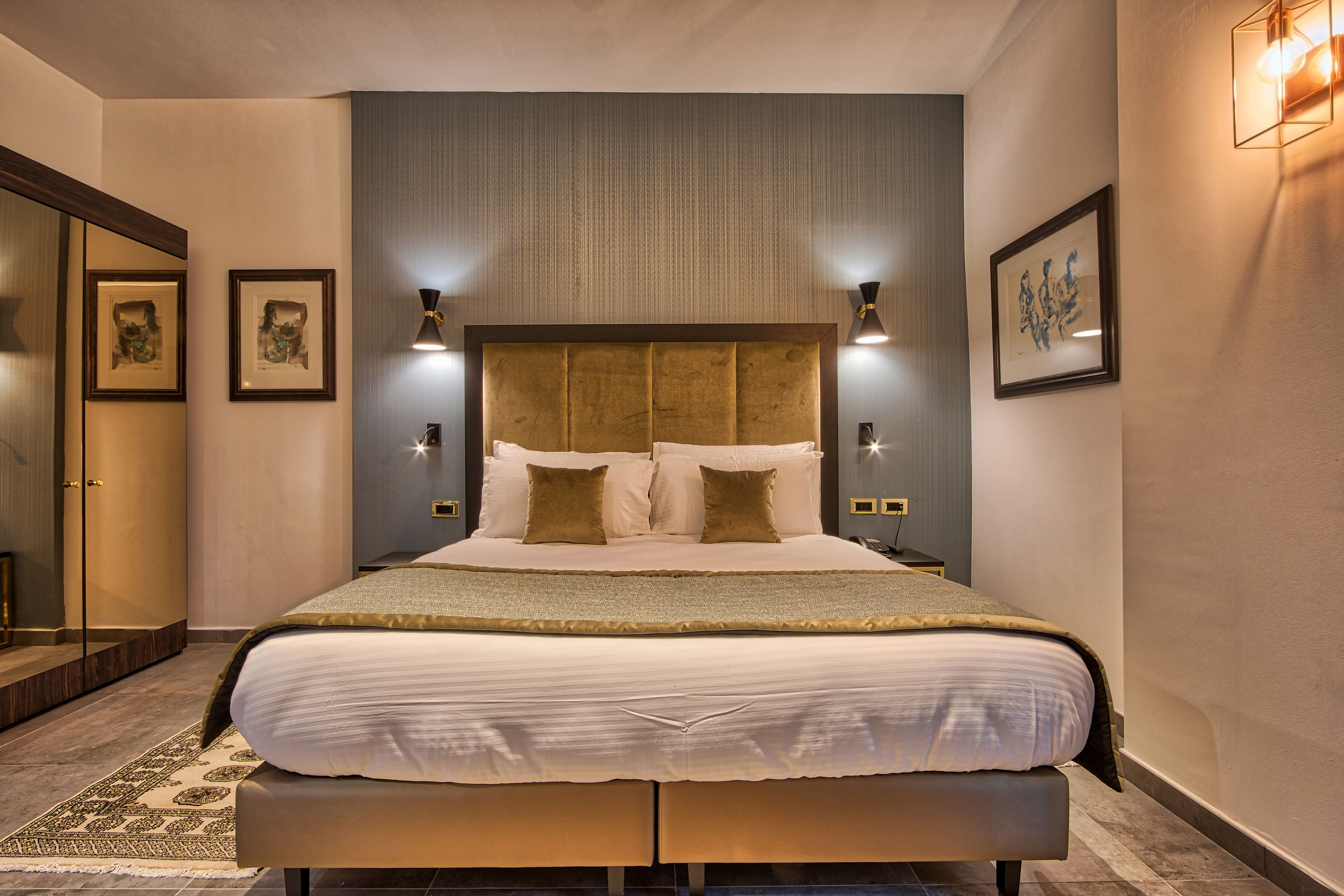 A modern hotel bedroom with a large bed, bedside lamps, and framed artwork on the walls.