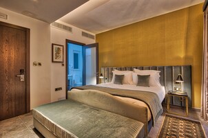 Una camera d'albergo moderna con un letto grande, un comodino con una lampada e vista sul corridoio.