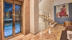 A hotel lobby with a marble floor, a staircase with a metal railing, and a painting on the wall.