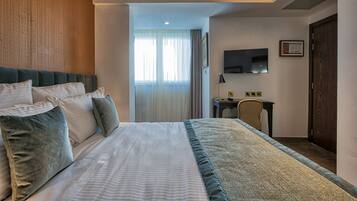 Habitación de hotel con una cama grande, un escritorio, una silla, un televisor y una ventana con cortinas.