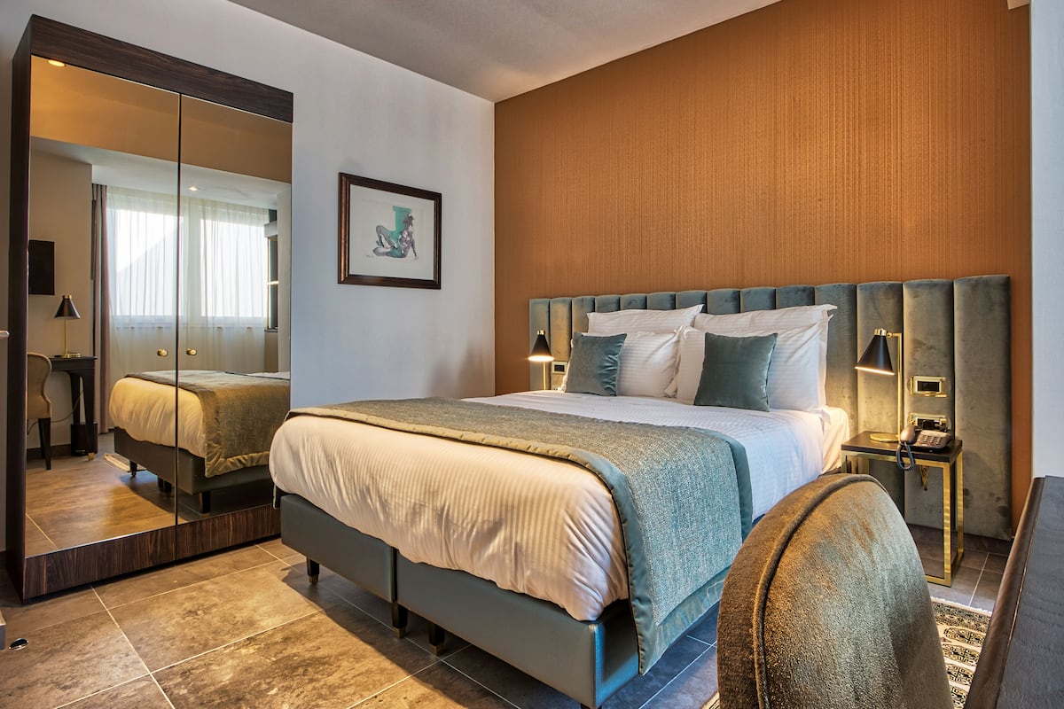 Ein modernes Hotelzimmer mit einem großen Bett, einem Spiegel, einem Nachttisch mit Lampe und einem gerahmten Bild an der Wand.