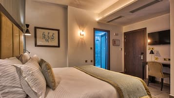 Habitación de hotel con cama, escritorio, silla, televisión y puerta que da a un balcón.