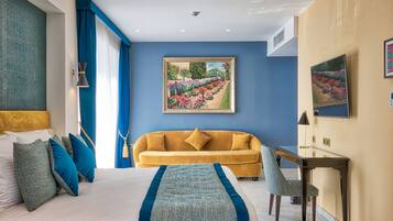 A hotel room with a bed, a sofa, a desk, and a painting on the wall.