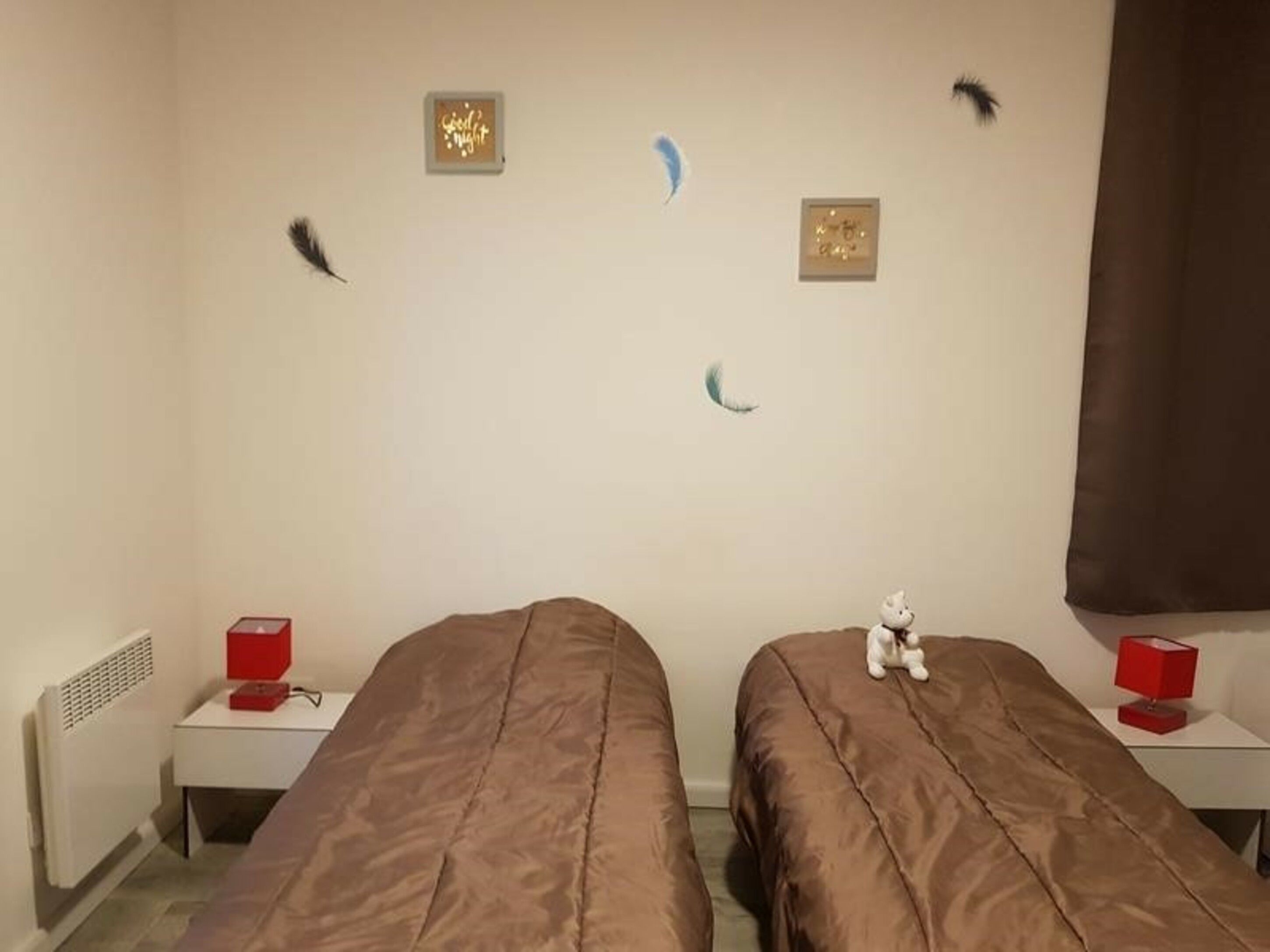 Una habitación con dos camas, un calentador y una pequeña mesa con una lámpara roja.