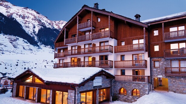 Een hotel met meerdere verdiepingen, balkons, een gevel van steen en een bord dat aangeeft dat het een skigebied is.