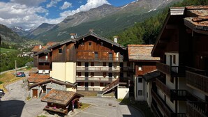A mountain lodge with multiple balconies, a parking area, and a view of the surrounding mountains. - Appart à 50m des remontées | Accès piscine + Sauna (Val-Cenis)