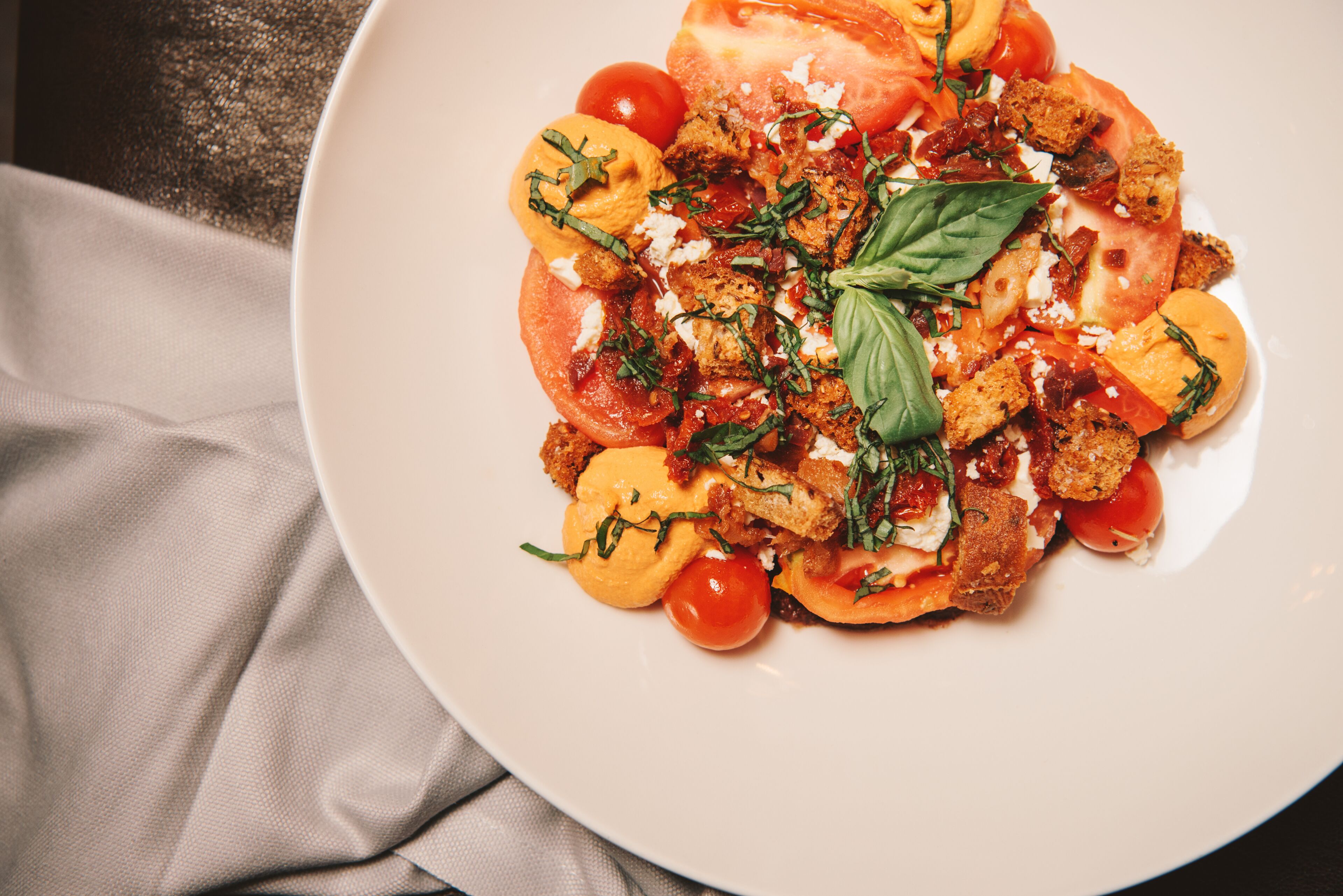 Un plato de comida con tomates, albahaca y crotones.