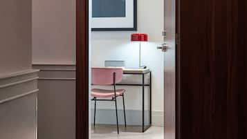 A hotel room entrance with a wooden door, a number '405' sign, a framed picture on the wall, a red lamp, and a pink chair.