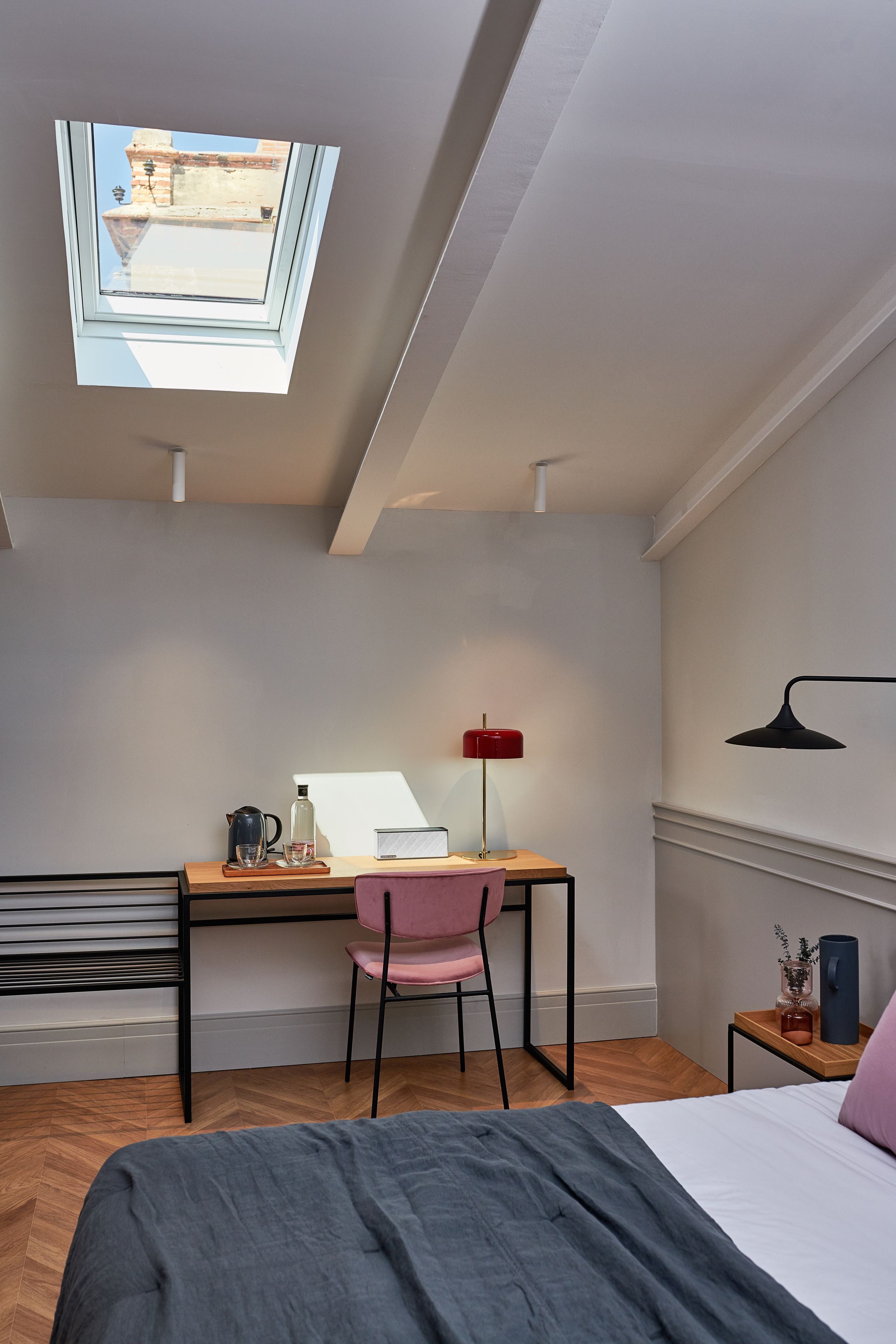 Een slaapkamer met dakraam, een bureau met stoel, een bed en een nachtkastje met lamp.