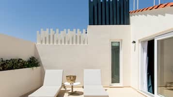 A rooftop terrace with two white lounge chairs, a small round table, and a basket.