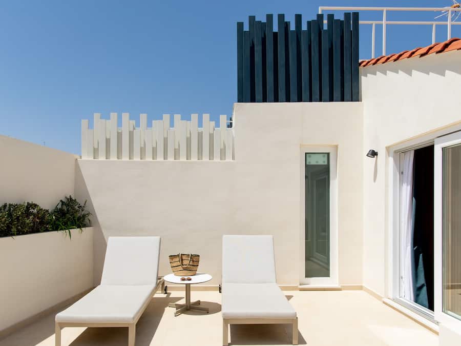 A rooftop terrace with two white lounge chairs, a small round table, and a basket.