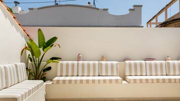 Un área de estar moderna al aire libre con un sofá a rayas blanco y beige, una planta grande y jarrones decorativos.