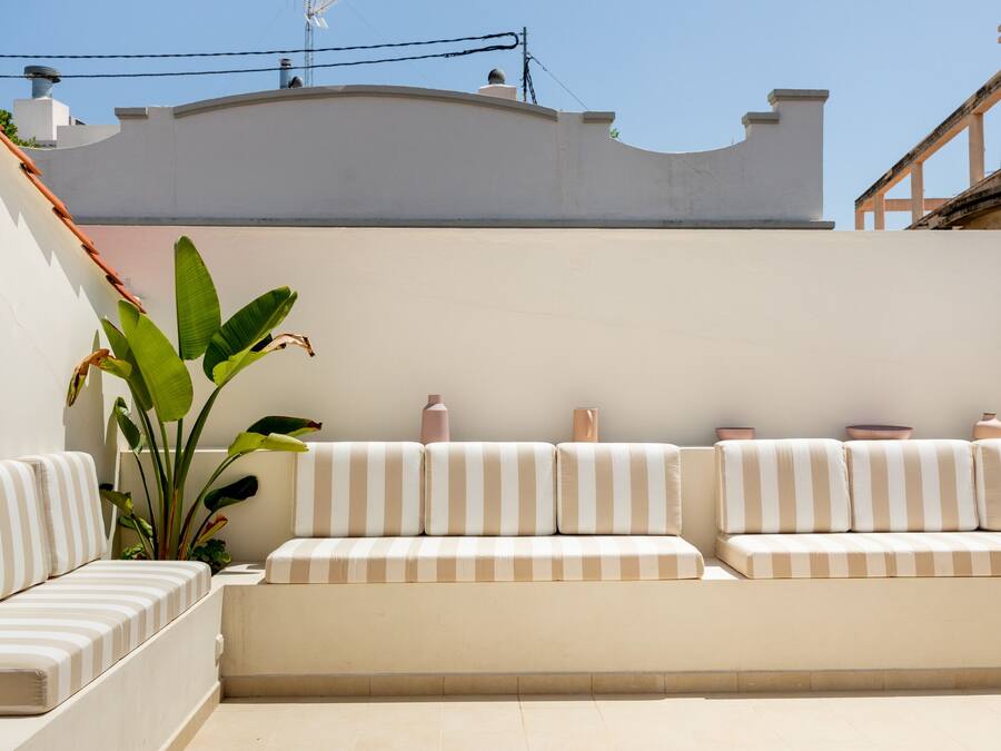 Un área de estar moderna al aire libre con un sofá a rayas blanco y beige, una planta grande y jarrones decorativos.