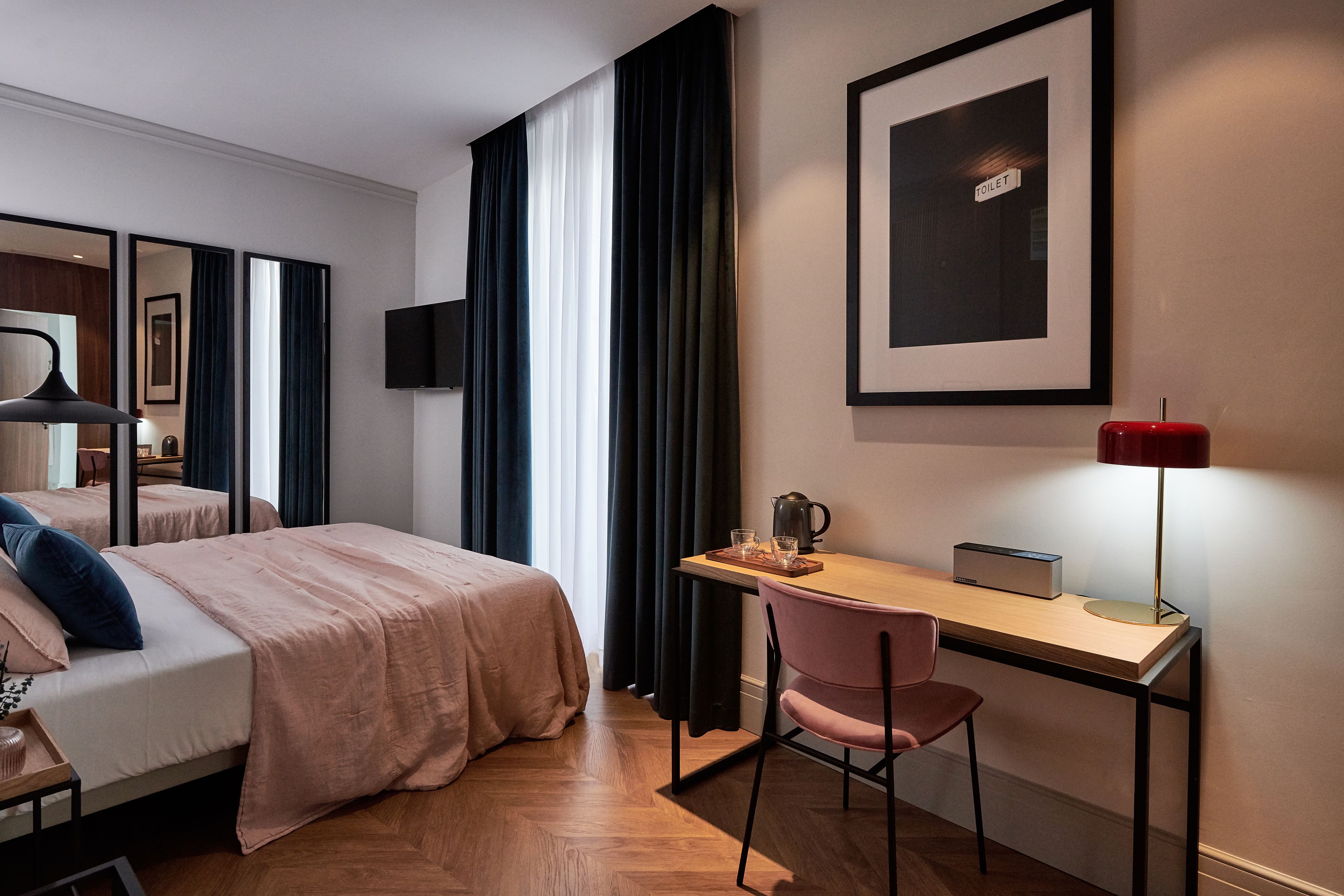 Una habitación de hotel con cama, escritorio, silla, televisor y un cuadro en la pared.