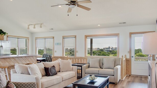 A spacious living room with a ceiling fan, large windows, and a view of the outdoors.