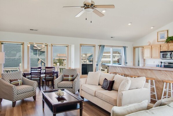 A spacious living room with a sofa, chairs, a coffee table, and a kitchen area with a bar counter.