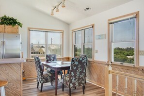 A dining area with a wooden table and floral chairs, large windows with views, and a kitchen with a refrigerator.