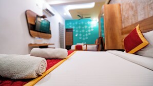 A hotel room with a bed, a red blanket, a white towel, a wooden headboard, and a teal wall with a floral pattern. - Hotel SDM Golden Tower (Rameshwaram)