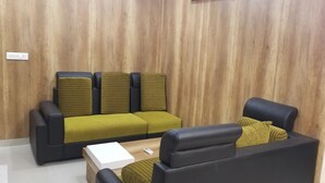 A modern living room with a wooden panel wall, a black sofa with green cushions, and a white coffee table. - Hotel SDM Golden Tower (Rameshwaram)