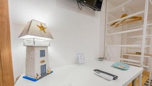 A room with a small lighthouse model, a white table, a remote control, and a clothing rack. - B&B Dimora del Pescatore Cefalù (Cefalù)