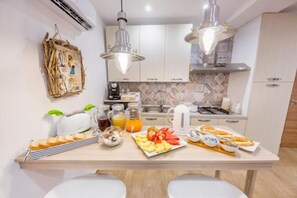 A modern kitchen with white cabinets, a central island with breakfast items, and pendant lighting. - B&B Dimora del Pescatore Cefalù (Cefalù)