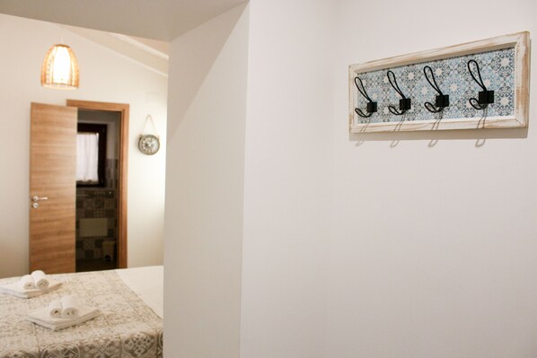 A hotel room with a bed, a wall-mounted towel rack, a wooden door, and a hanging light fixture. - B&B Dimora del Pescatore Cefalù (Cefalù)
