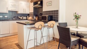 Una cocina moderna con armarios blancos, encimera negra y una isla central con taburetes de bar. Se observa un microondas, tostadora y una viga de madera sobre la estufa.