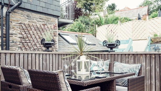 Un patio con mobiliario de mimbre, una mesa de vidrio y plantas en macetas.