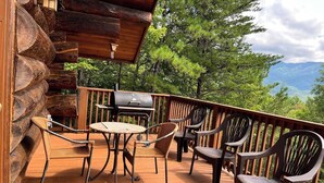 A wooden deck with a grill, chairs, and a table. - Infinite Views - 2BR/New Hot Tub/New Firepit/Grill/Sleeps 6 (Gatlinburg)