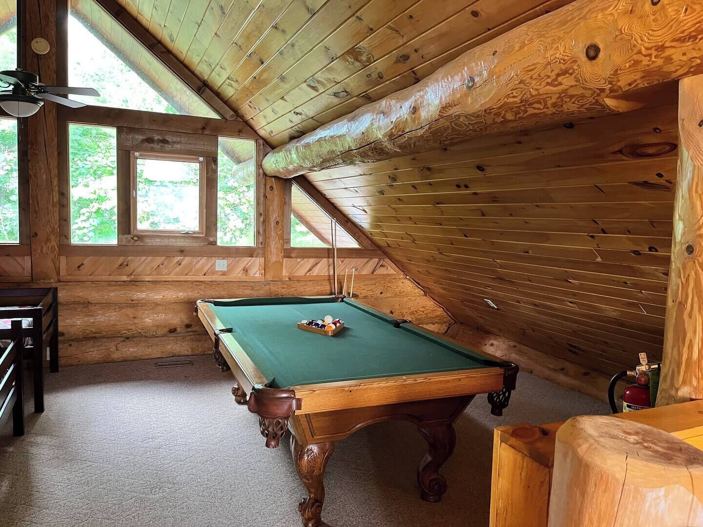 A wooden room with a pool table, a ceiling fan, and large windows.