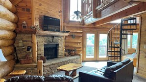 A log cabin interior with a stone fireplace, leather sofas, and a spiral staircase. - Infinite Views - 2BR/New Hot Tub/New Firepit/Grill/Sleeps 6 (Gatlinburg)