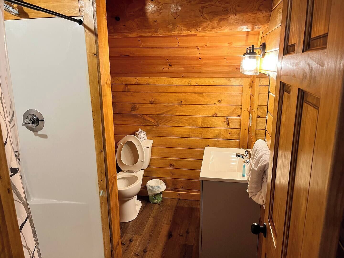 Ein Badezimmer einer Holzhütte mit Toilette, Waschbecken und einem Handtuch, das an der Tür hängt.