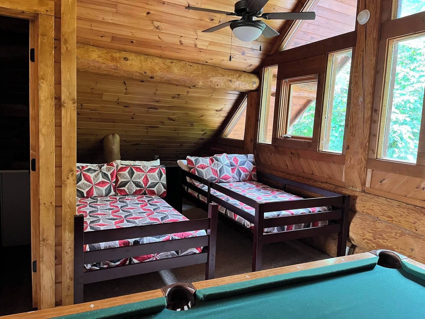 Een gezellig chalet met twee stapelbedden, een plafondventilator en een pooltafel.