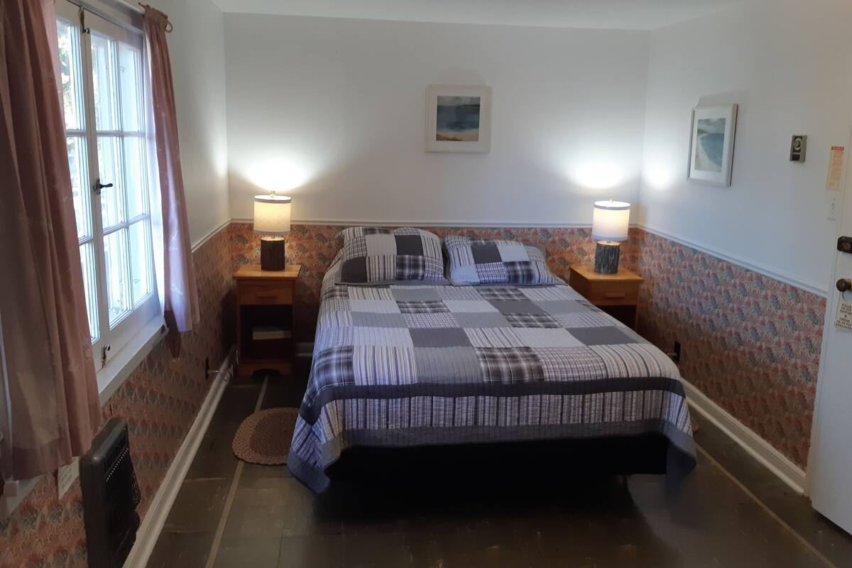 A bedroom with a bed, two bedside lamps, a window with curtains, a rug, and a wall with a floral pattern.