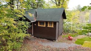 A small wooden cabin with two windows, surrounded by trees and a gravel path. - Miners Bay Lodge (Minden Hills)