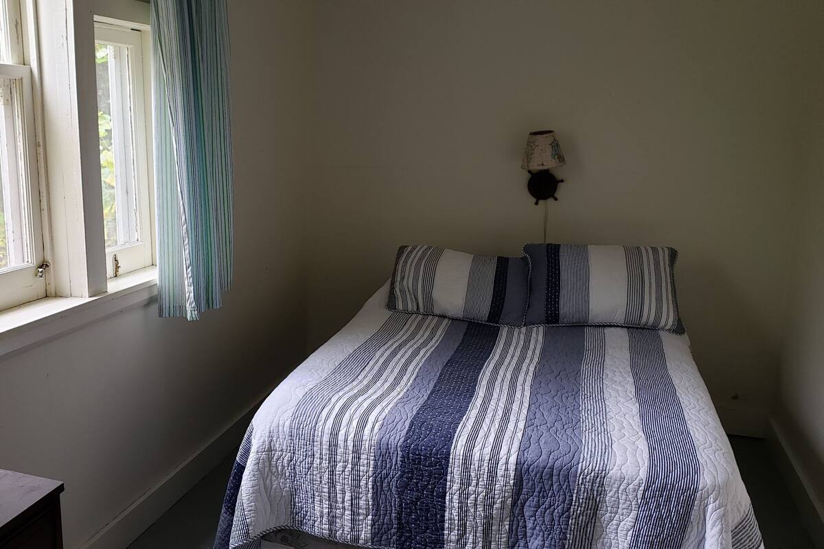 A bedroom with a bed, a window with curtains, and a wall-mounted lamp.