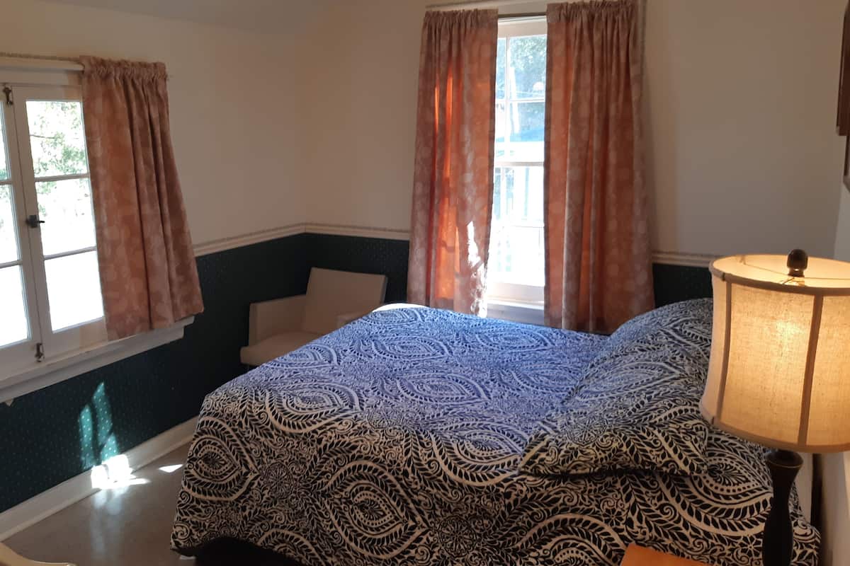 A bedroom with a bed, a chair, a window with curtains, and a lamp.