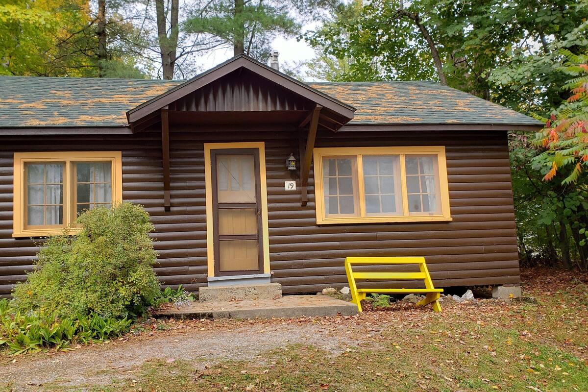 A log cabin with a front porch, a bench, and a number 19 sign.