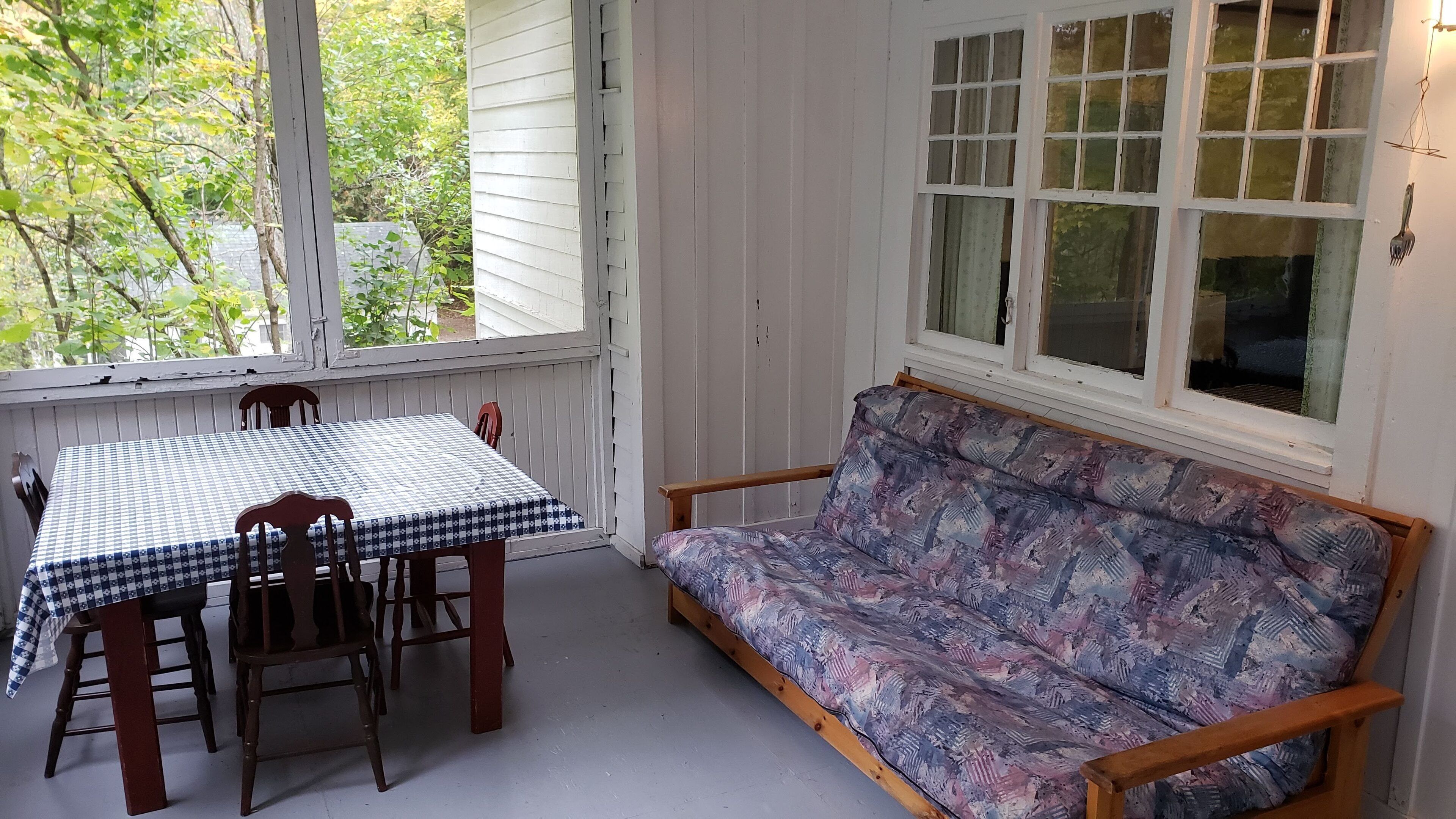 Eine überdachte Veranda mit Tisch und Stühlen, einer Holzbank und einem Fenster mit vielen Glasscheiben.