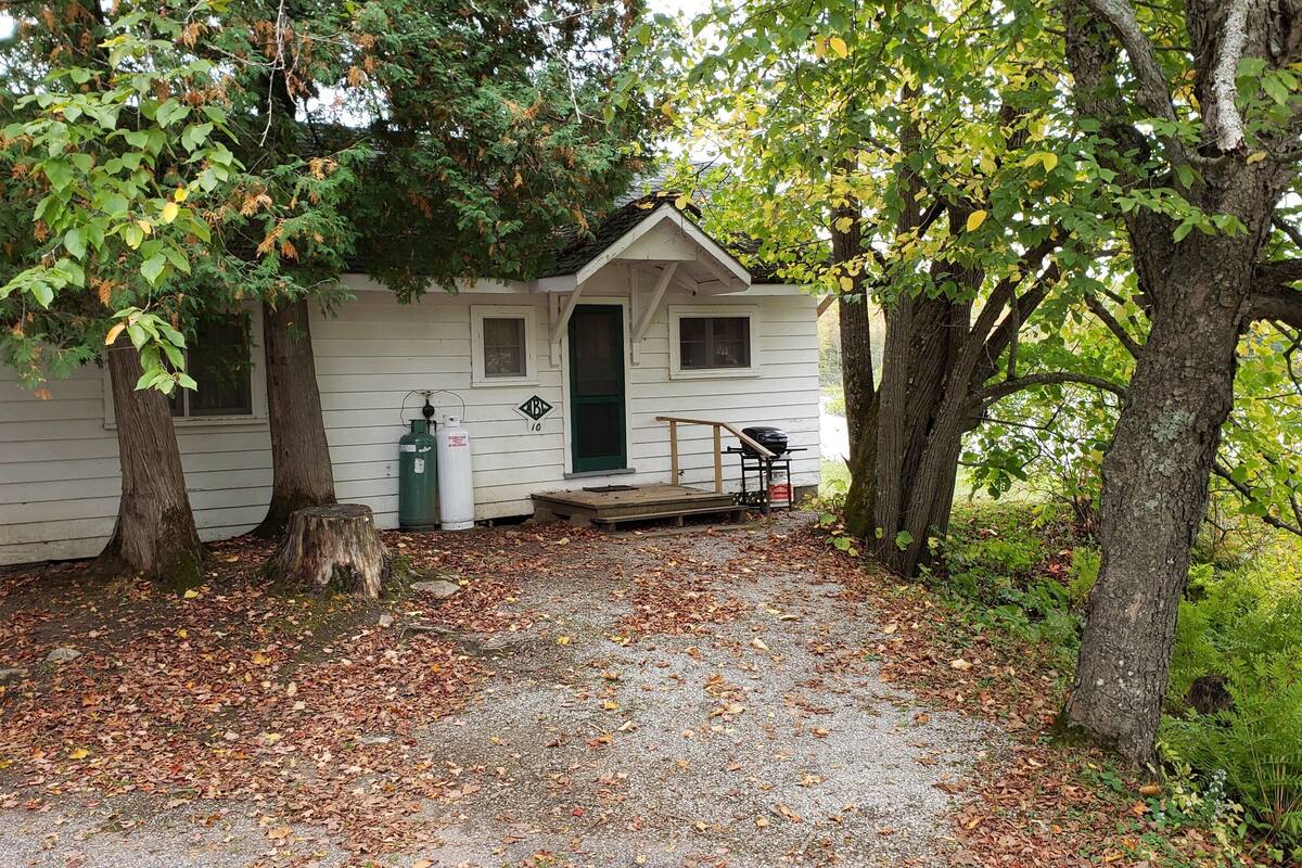 A small cabin with a porch, a grill, and propane tanks outside.