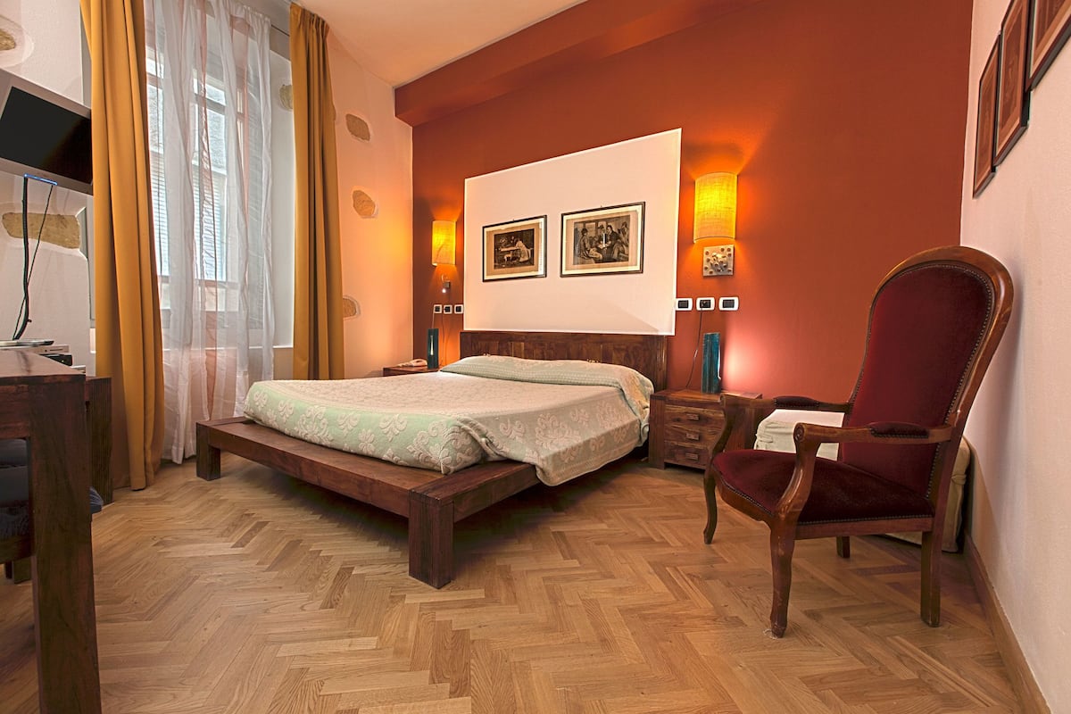 Un dormitorio con una cama de madera, una silla roja, un televisor y dos lámparas fijadas a la pared.